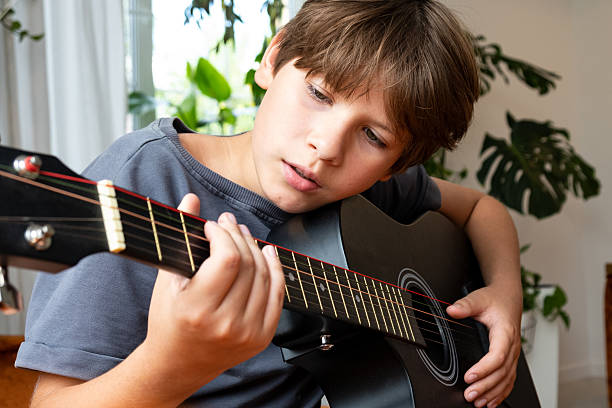 istock Young boy playing an acoustic guitar indoors, focused on pressing strings and fretboard 2249382038