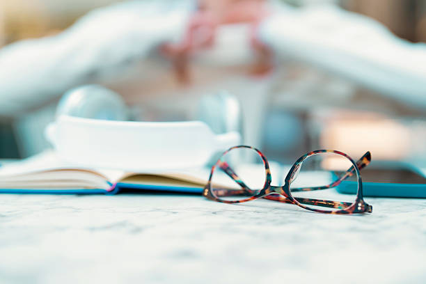 A person sits at a cafe table, reading a book while sipping coffee. Glasses rest nearby, creating a relaxed atmosphere perfect for enjoying literature.