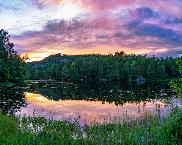 Scandinavian lake landscape with forest reflections and colorful sunset sky in summer Sweden