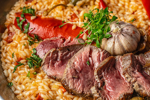 Gourmet paella with juicy medium-rare beef slices, roasted garlic and vegetables, rich Spanish rice close-up, top view food background