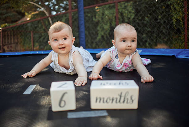 Twin baby girls lying on a trampoline with 6 months blocks, celebrating a development milestone