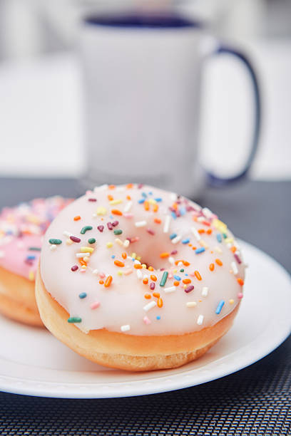 View of two vanilla and pink glaze donuts with colorful sprinkles on a plate