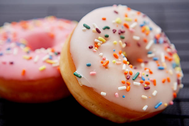 Close-up of two vanilla and pink glaze donuts with colorful sprinkles