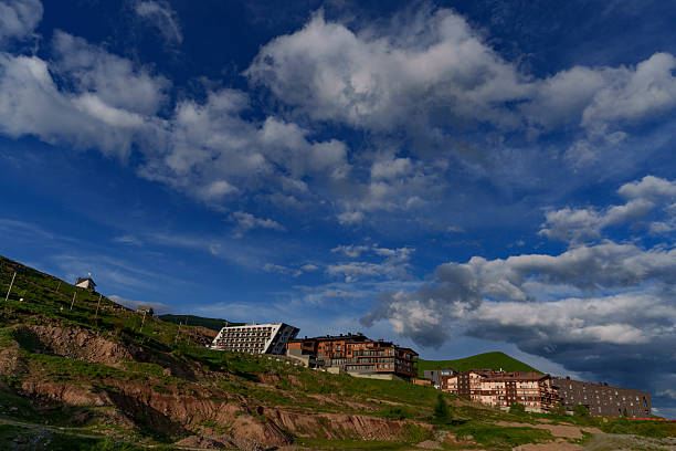 Mountain resort hotels scattered along grassy slope beneath expansive deep blue sky with fluffy clouds
