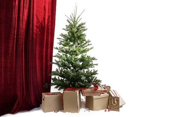 istock Christmas tree without decorations, underneath many cardboard boxes for gifts ready to be wrapped, red curtain on the left, right side against a white background, copy space 2249395880