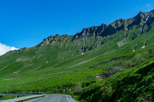 istock Empty mountain road leading toward rugged green ridge and blue sky 2249396129