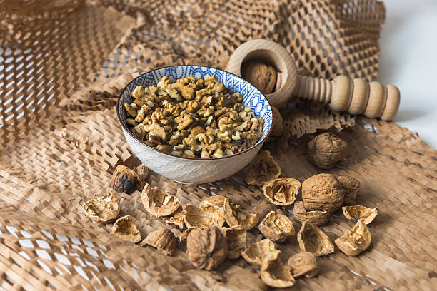 A dynamic, high-angle shot capturing the process of cracking walnuts. A blue and white patterned bowl is centrally positioned, filled with shelled kernels