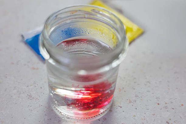 istock Close-up shot of a glass jar containing water, into which bright red Easter egg dye is being poured or dissolved. Concentrated color is visible at the bottom of the jar, dissolving into the water. 2249404542