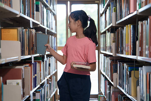 Young girl reading book in library filled with shelves, where education brings happiness and joy to every page.