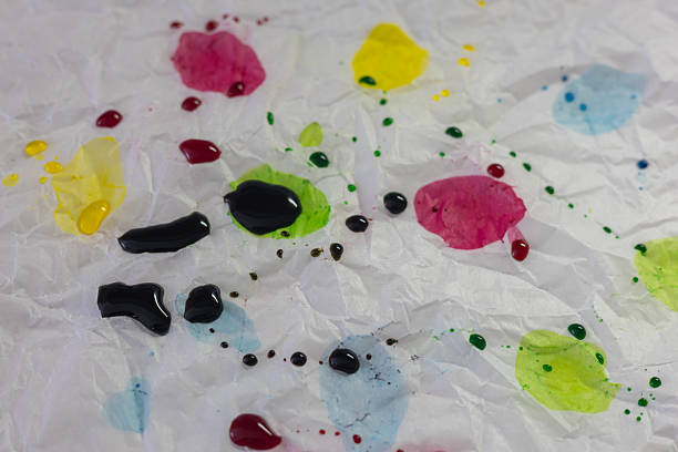 An abstract close-up shot of crumpled white paper or plastic surface, splattered with drops and stains of bright egg dyes  red, yellow, green, and blue, including small dark color splatters.