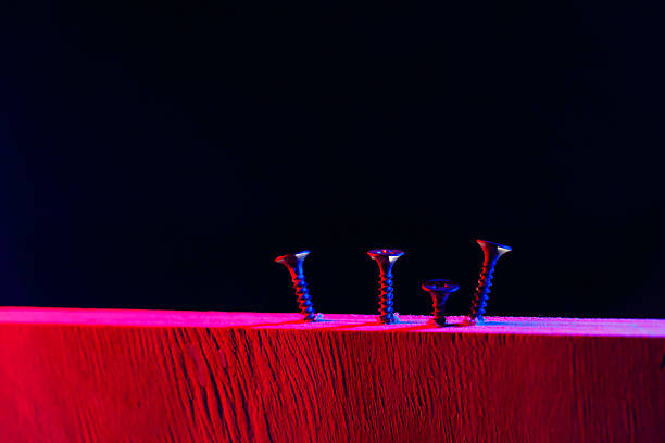 Screws screwed into a wooden beam in hard red light