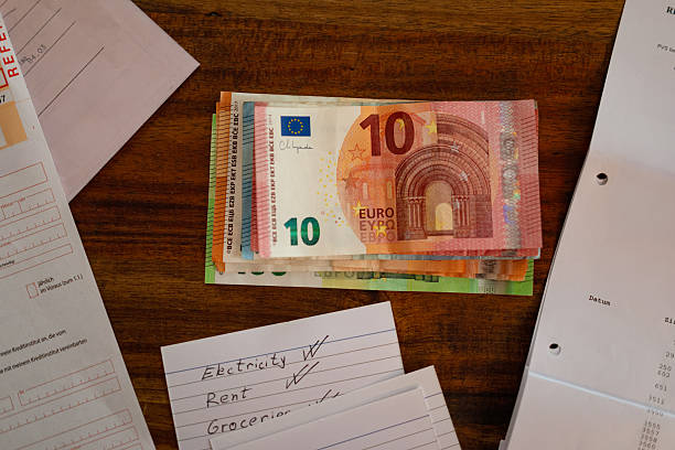 Close-up shot of euro banknotes neatly stacked on a wooden table next to handwritten expense notes for electricity, rent, and groceries, showing everyday budgeting and financial planning.