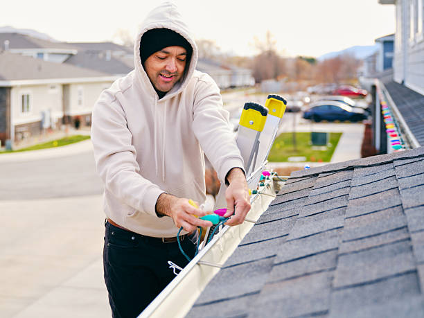 A hispanic man standing on a ladder, hanging Christmas lights on the outside of his home.