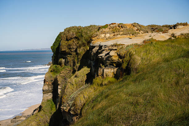 Steep grassy coastal cliff rises above the Atlantic Ocean shoreline at Cabo da Roca Sintra District of Lisbon Portugal in autumn daylight.