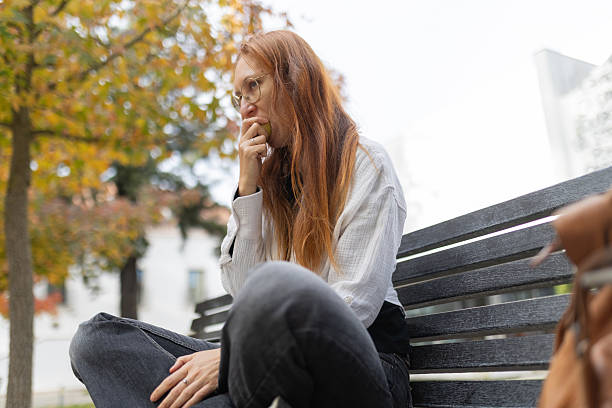 istock Young woman eating apple having thoughtful moment on bench 2249417496