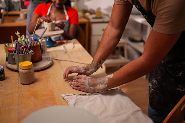 istock Potter kneading clay on a wooden table in a workshop, preparing it for shaping and creating pottery, with another potter working in the background 2249419642