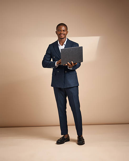 istock Man in pinstripe suit holding a laptop while standing in studio 2249426380