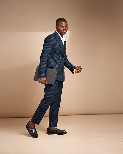 istock Man in pinstripe suit walking while holding a laptop in studio 2249426883