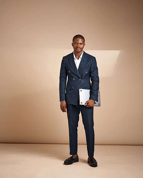 istock Man in pinstripe suit standing and holding a closed laptop in studio 2249426887