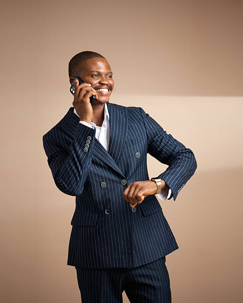 istock Smiling man in pinstripe suit talking on phone and checking time in studio 2249427431