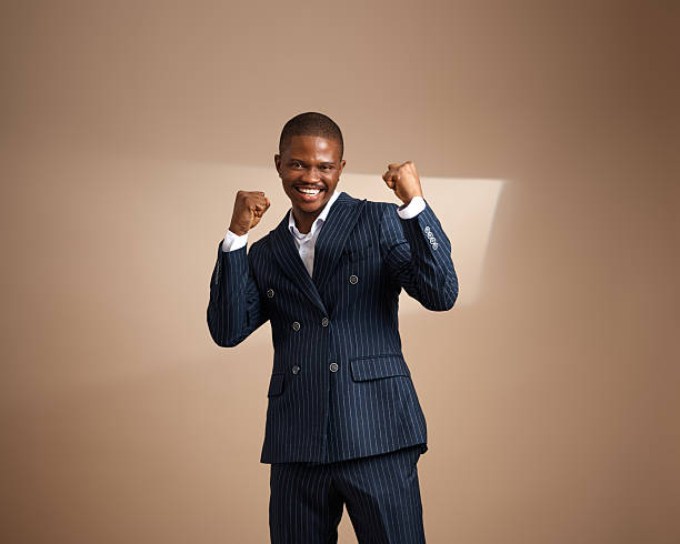istock Smiling man in pinstripe suit posing with raised fists against plain background 2249428042