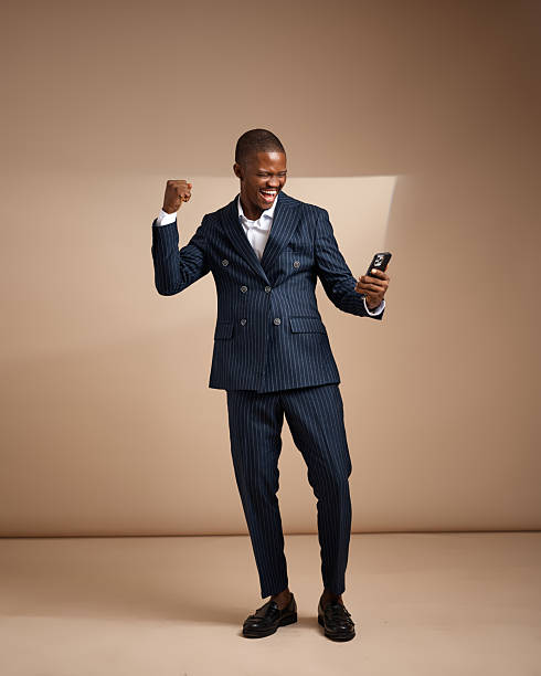 istock Man in pinstripe suit celebrating while looking at smartphone in studio 2249428043