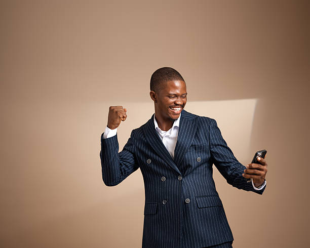 Man in pinstripe suit celebrating while looking at smartphone in studio