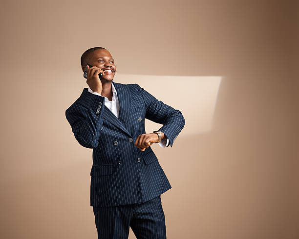 Man in pinstripe suit smiling while talking on phone and checking watch