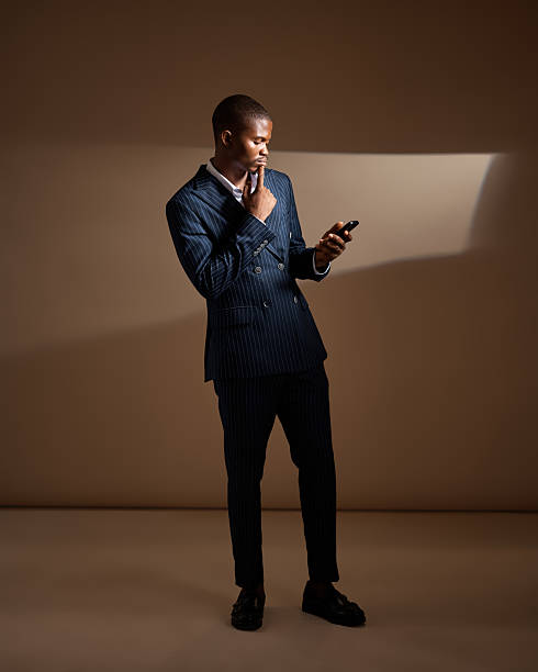 istock Man in pinstripe suit looking at phone while touching chin in studio 2249428234