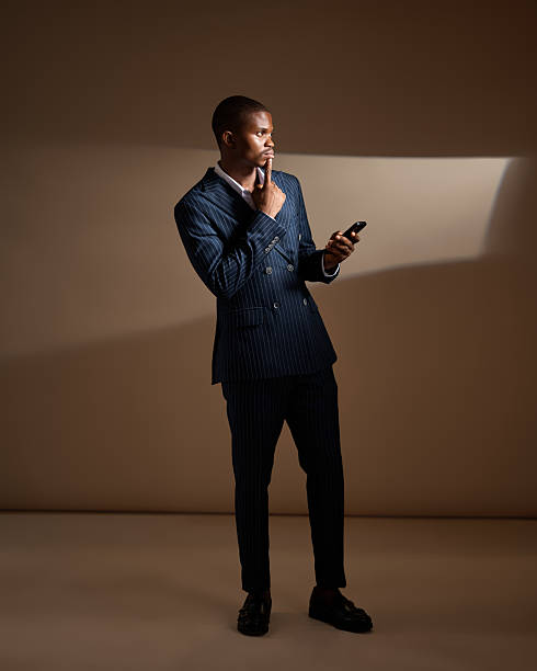 istock Man in pinstripe suit holding phone and touching chin in studio 2249428265