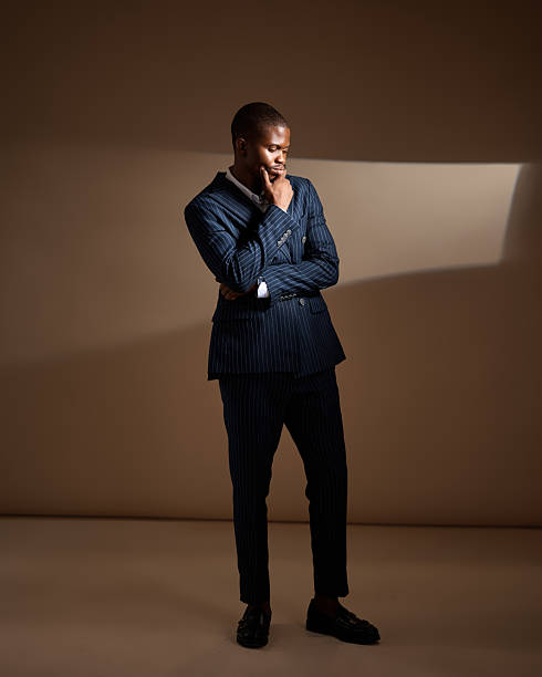 istock Man in pinstripe suit standing with hand on chin in dramatic studio lighting 2249428432