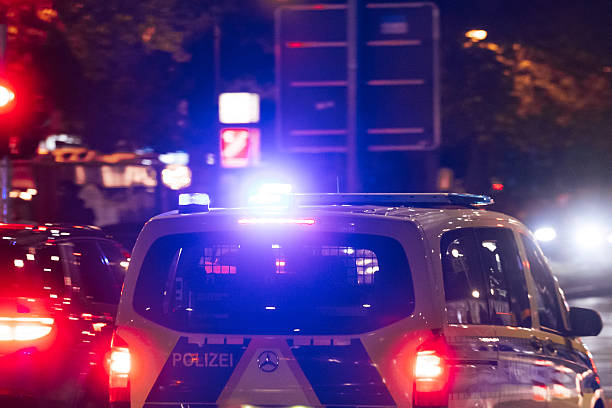 Berlin, Germany – October 29, 2025: A German Polizei patrol vehicle with activated blue lights moves through evening traffic on a city street. Surrounding cars and illuminated signs are visible in the blurred night environment.
