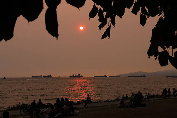 A dramatic sunset over the water, with several ships visible on the horizon during British Columbia wildfires.