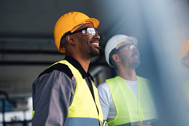 istock Smiling Construction Workers In Hard Hats And Safety Vests On A New Office Build Site 2249439287