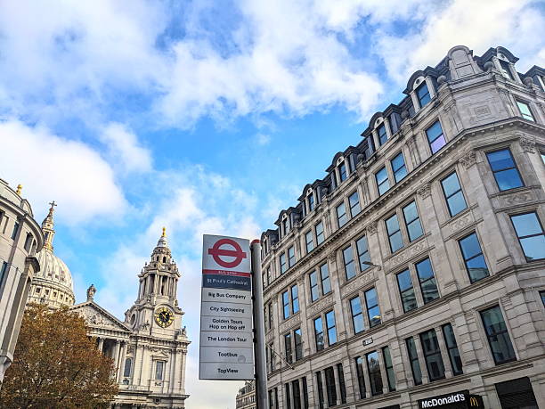 London, UK - November 08 2025: A low angle view captures the iconic dome of St Paul's Cathedral next to a classic red bus stop sign, set against a backdrop of historic architecture and a blue sky
