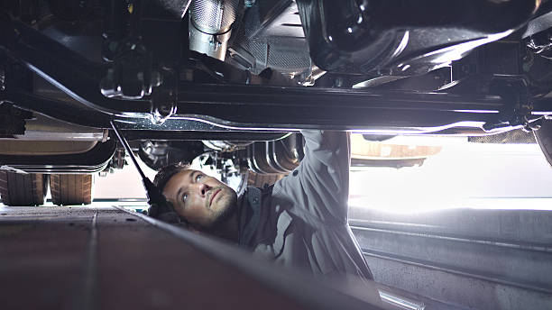 istock Low Angle View of Mechanic Inspecting Car Undercarriage in Garage 2249447467