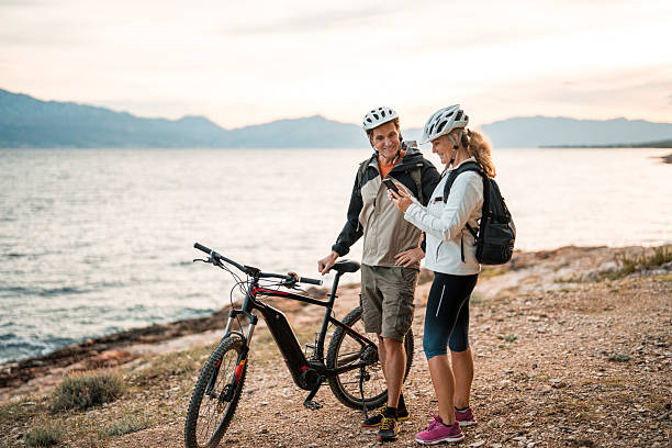 istock Senior Couple with E-Bikes Checking Smartphone by Ocean at Dawn 2249449178