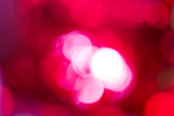 Abstract defocused lights. Blurred circles of white and bright pink light against deep red background, creating dynamic bokeh effect. This soft, defocused view provides colorful, festive atmosphere