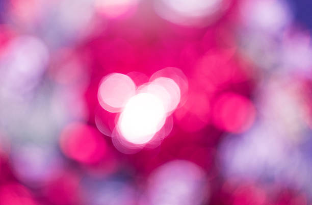 Defocused photography features bokeh effect dominated by pink and magenta colors. Blurred circles of light overlap, with cluster of bright white circles centered in the frame. Abstract background