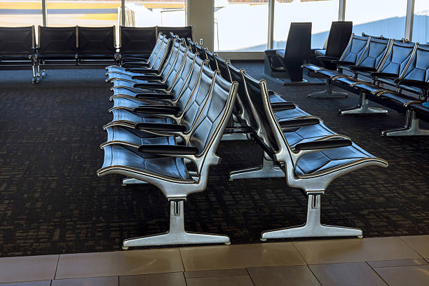 Rows of empty metal leather seats fill bright airport waiting area, inviting travelers to relax wait.