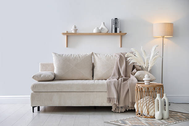 istock Comfortable sofa with pillows, blanket, lamp and different decor near white wall indoors 2249453391