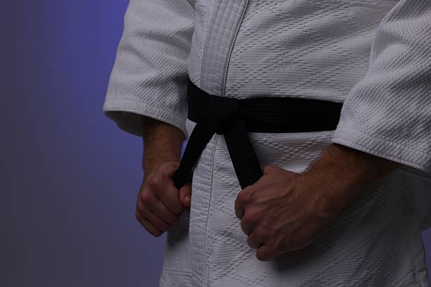 Karate fighter in uniform on dark purple background, closeup