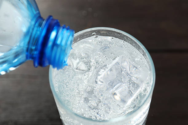 istock Pouring refreshing soda water from bottle into glass at dark table, closeup 2249455280