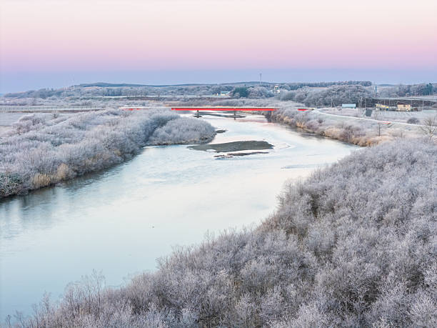 A red bridge stands out against a white frozen lake landscape with pink dawn sky in north Hokkaido.