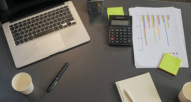 Busy business work meeting project planning setup on desk, featuring laptop, calculator, charts, notebook, pen, colorful sticky notes, paper cups.