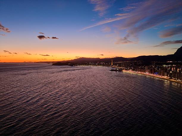 sunset bay aerial with gentle ripples, small boats and distant illuminated shoreline, warm gradient sky