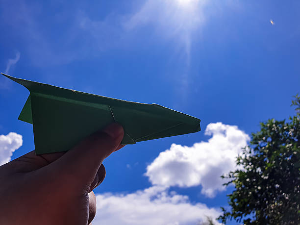 Close up of a senior man wearing retro style pilot costume with blue cloudy sky in background. He is holding model paper plane in hand and is looking up while he is daydreaming. Representing active senior adult concept.