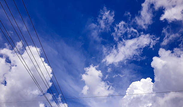 Urban sky view featuring power lines crossing bright clouds against deep blue sky, useful for infrastructure themes, modern environment visuals, and open background layouts.