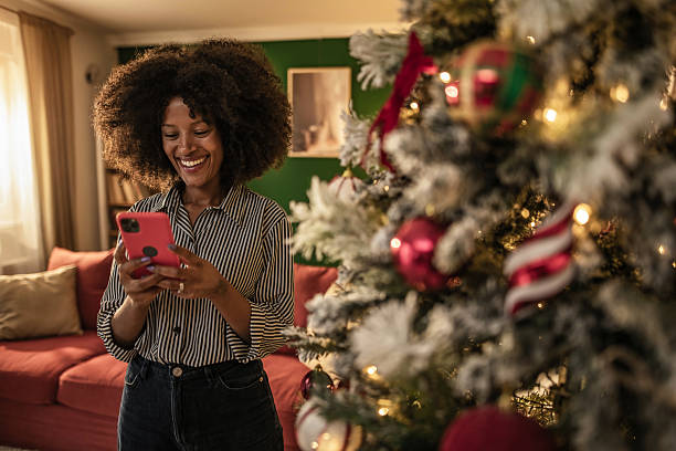 istock Young black woman using phone next to Christmas tree at home on Christmas 2249479665