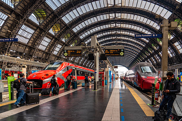 A train parked at the platform at the Milan, Italy train station.   Black and white.   High arch ceiling.
